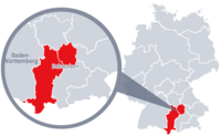 Diese Grafik zeigt eine Karte von Deutschland mit einer detaillierten Ansicht der Region Schwaben. Schwaben ist in Rot hervorgehoben und liegt im südlichen Teil Deutschlands. Ein Lupensymbol vergrößert diesen Bereich, um die Lage genauer darzustellen. 